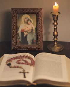 an open book sitting on top of a table next to a candle and a picture