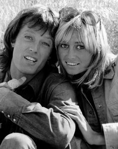 a man and woman sitting next to each other in front of a field with tall grass