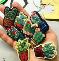 a hand is holding several embroidered patches with small cactuses in them and flowers on them