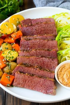 a white plate topped with meat, potatoes and carrots next to lettuce