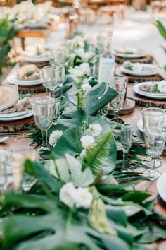 the table is set with plates, glasses and greenery for an elegant dinner party