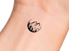 a small tattoo on the wrist of a person with mountains in the background and trees