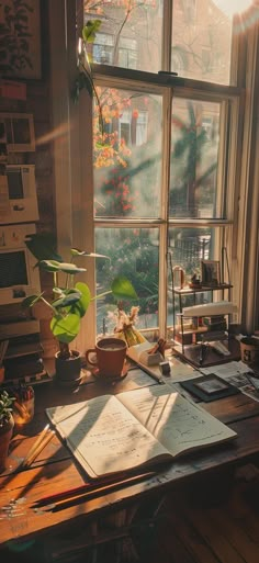 an open book sitting on top of a wooden table next to a window filled with plants