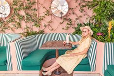 a woman sitting at a table in front of a wall with flowers and plants on it