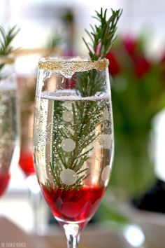 two wine glasses filled with liquid and decorated with evergreen branches, snowflakes and dots