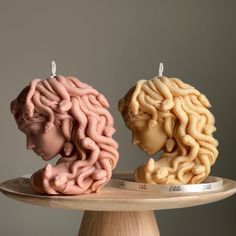 two candles shaped like human heads sitting on top of a cake plate