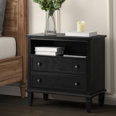 a black night stand with two drawers and a vase filled with flowers next to a bed