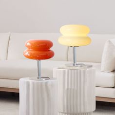 two lamps sitting next to each other on top of white pedestals in front of a couch