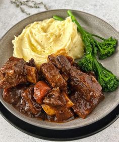 a plate topped with meat and mashed potatoes next to broccoli on a table