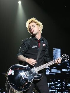 a man with blonde hair playing an electric guitar in front of a microphone on stage