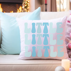 two pillows sitting on top of a white couch next to a christmas tree with pink and blue ornaments