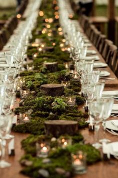 a long table covered in moss and lit candles is set with place settings for dinner