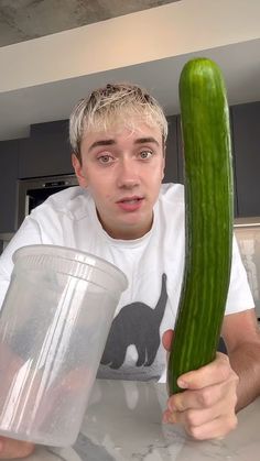 a young man holding a large cucumber in his hand while looking at the camera