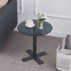 a glass table with a flower vase on it next to a couch and coffee cup