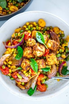 a white bowl filled with vegetables and tofu on top of a table next to another bowl