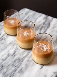 three glasses filled with dessert sitting on top of a marble table