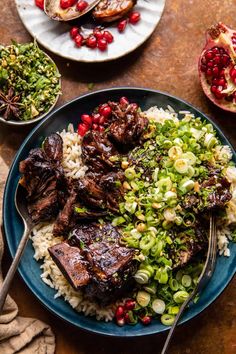 a blue plate topped with meat, rice and pomegranates next to other dishes