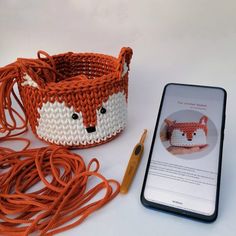 an orange and white knitted basket next to a cell phone with the app on it