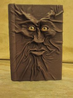 a brown leather book with an evil face on it's cover, sitting on a wooden table