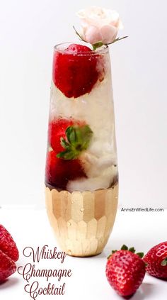 a glass filled with ice and strawberries on top of a white table next to some strawberries