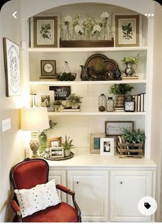 a white book shelf filled with lots of books and plants next to a red chair