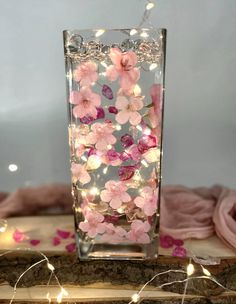 a vase filled with pink flowers on top of a wooden table covered in fairy lights