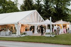 a group of people standing outside of a white tent