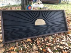 a black wooden sign sitting on top of leaves in front of a tree and fence