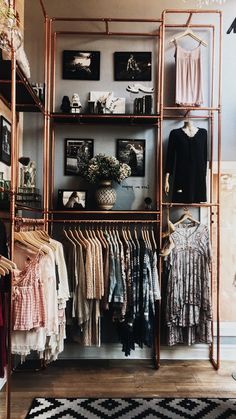 a clothing rack with clothes and pictures on the wall in a room filled with other items