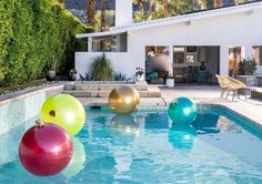 some balls are floating in the water near a swimming pool with chairs and tables around it