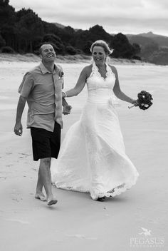 a bride and groom walking on the beach holding hands, black and white photo with trees in background