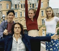 the cast of friends posing for a photo in front of an old building with their arms up