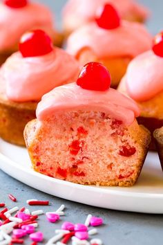 cupcakes with pink frosting and cherries on a plate next to sprinkles