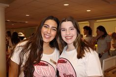 two young women standing next to each other in front of a room full of people