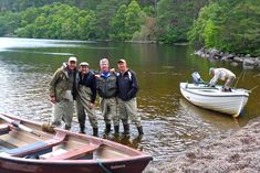 three men standing in the water next to two canoes and a boat on the shore