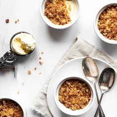 three bowls filled with dessert sitting on top of a white table next to spoons