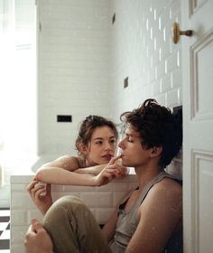 a young man and woman sitting on the floor in front of a bathroom mirror looking into each other's eyes