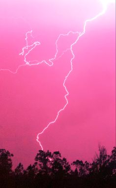 a pink sky with lightning striking through the clouds and some trees in the foreground