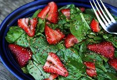 a salad with strawberries and spinach in a blue bowl next to a fork