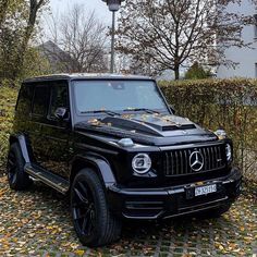 a black mercedes g - class parked in front of a hedge