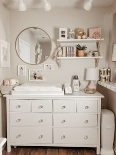 a baby's room with a dresser, mirror and shelves on the wall above it