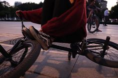 the person is riding their bike on the sidewalk near other people in the city at sunset