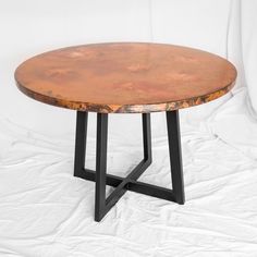 a round wooden table sitting on top of a white sheet covered floor next to a black metal frame