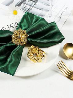 a white plate topped with two napkins and gold forks next to a green satin bow