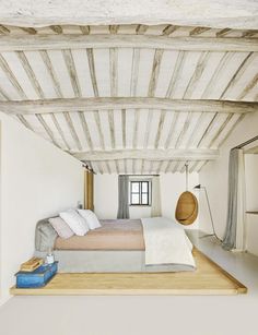 a bed sitting in the middle of a room under a wooden beam with pillows and blankets on it