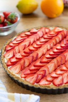 a pie with sliced strawberries on it sitting on a table next to lemons and oranges