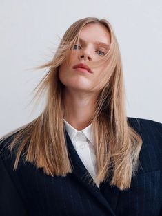 a woman with long blonde hair standing in front of a white wall wearing a suit