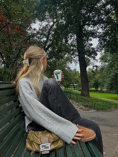 a woman sitting on top of a green bench next to a park filled with trees