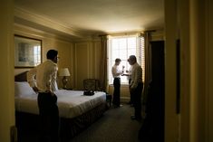 two men standing next to each other in a room with a bed and lamps on