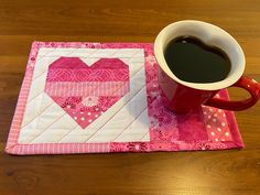 a cup of coffee sitting on top of a table next to a heart shaped quilt